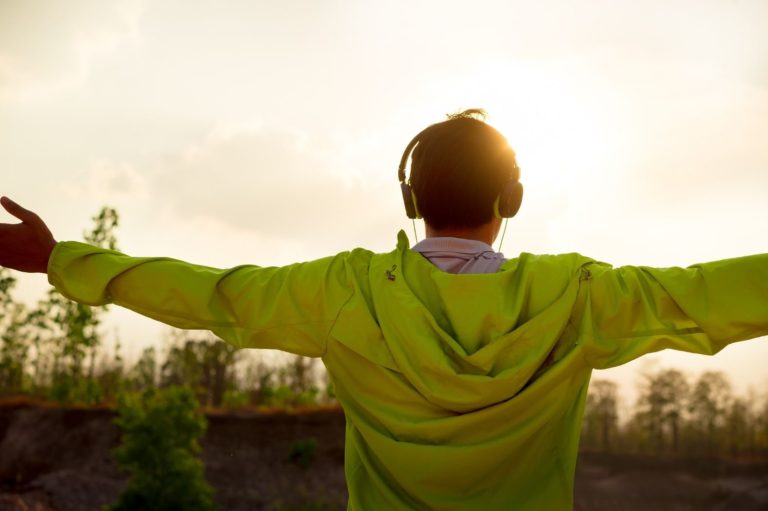 Back of a person in a lime jacket, wearing headphones, and holding their hands out horizontally.