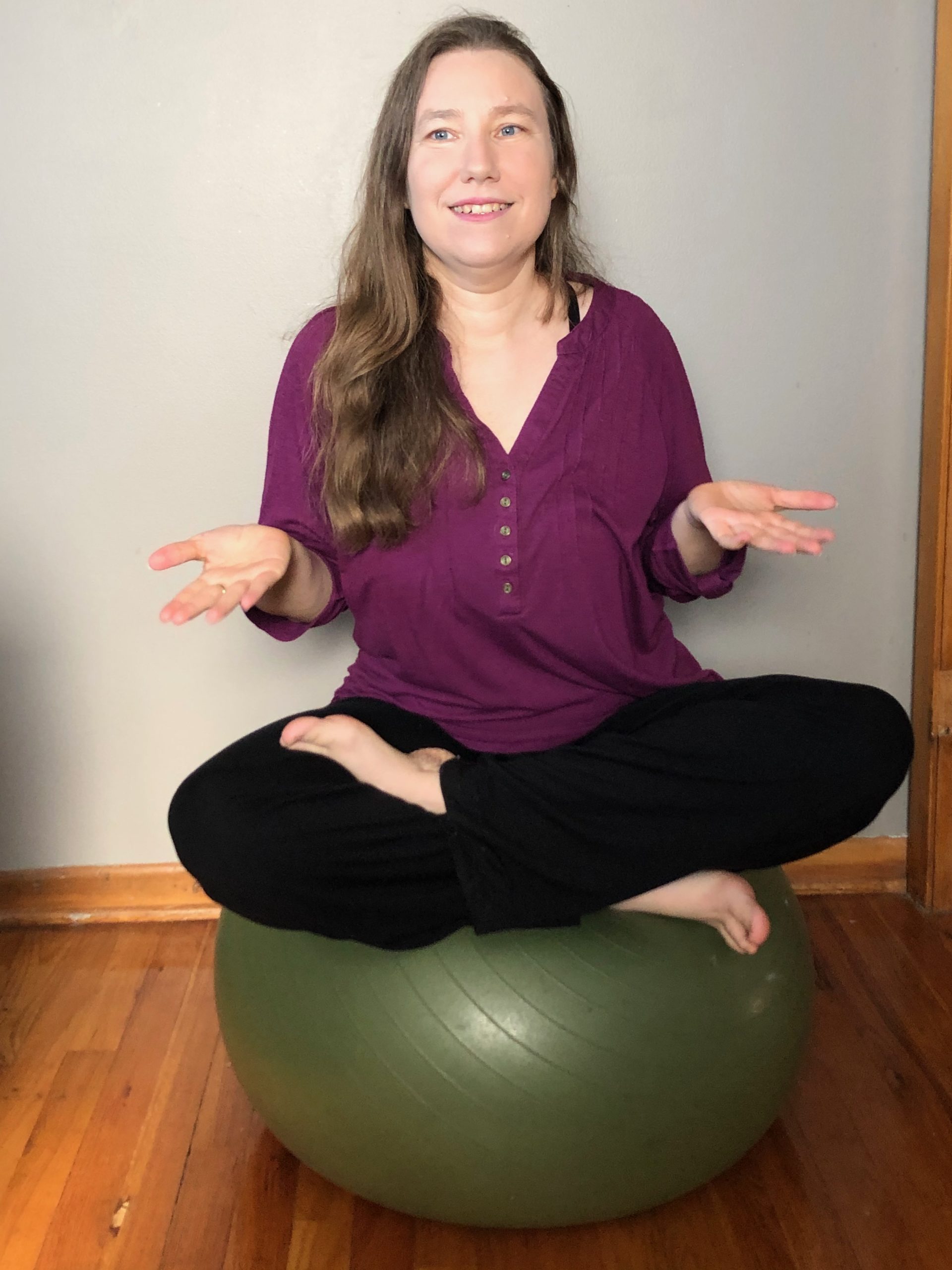 Women in a red shirt, shrugging while sitting cross-legged on a green yoga ball.