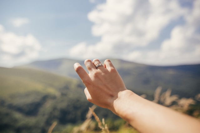 Close-up on a hand reaching towards green mountains.