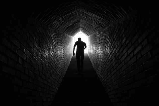 A person walking up a shaded stairwell into light.