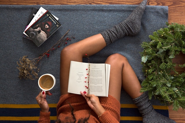 Someone resting a book on their lap while holding a cup of hot chocolate.