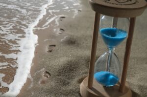 Hourglass rested on the shore nearby footprints.