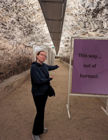 A person in a blue hoodie gesturing towards a tunnel with a sign that reads, "This way... out of burnout."