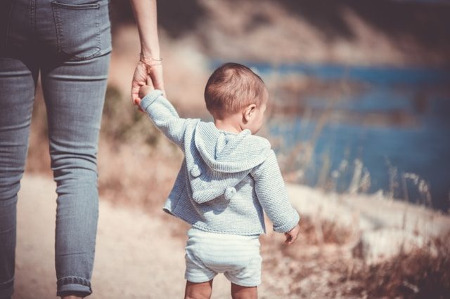 Parent holding their child's hand, while the kid looks to a lake in the distance.