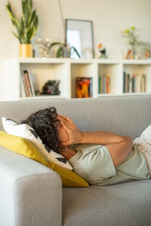 A person laying on a couch, holding their hands over their face.