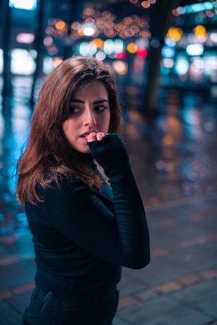 Person chewing on their fingernail in front of blurred city lights.