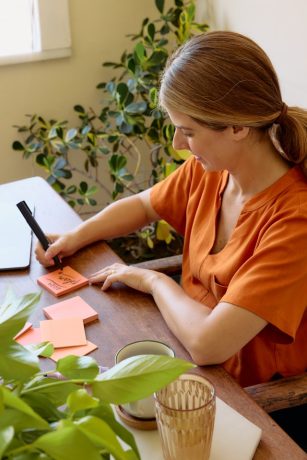 A person sitting at a desk and writing on an orange sticky note.