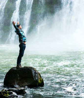 Someone stretching on a rock while looking towards a waterfall.